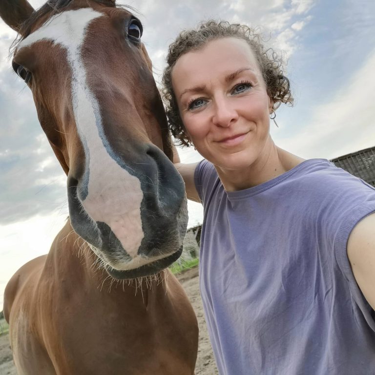 Frau posiert lächelnd mit einem braunen Pferd 