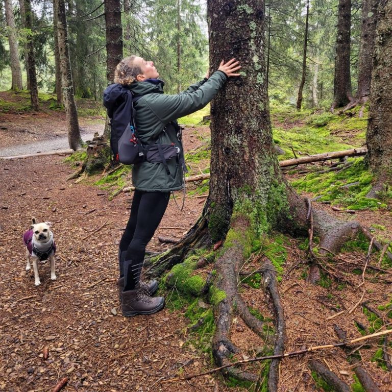 Person mit Hund in einem Wald, der einen Baum berührt.
